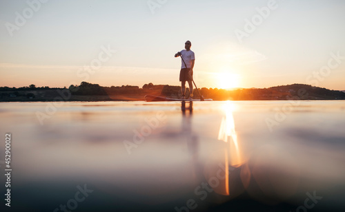 Man paddling SUP board on the lake at sunset