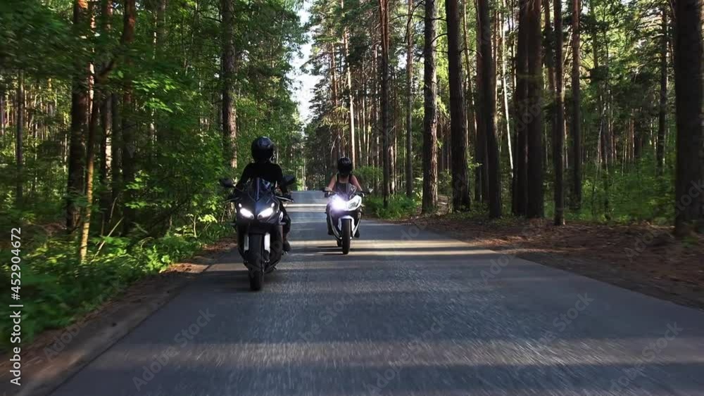 Two women riding motorcycles on the empty narrow road in the forest at summer Two women riding motorcycles on the empty narrow road in the forest at summer