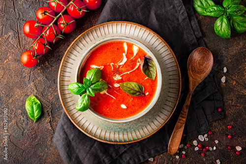  A bowl of traditional Spain tomato soup with cream and basil on the dark background top view. Tomato and basil gazpacho in a gray bowl