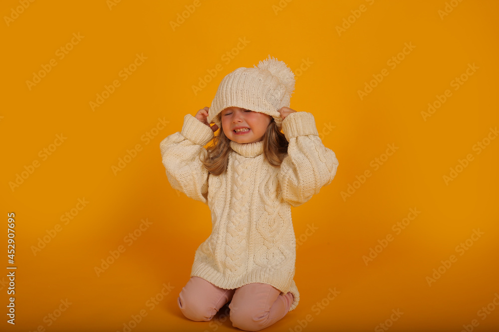 beautiful little blonde girl in a winter knitted white hat sweater and socks new year on a yellow background