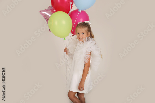 beautiful blonde girl in a white dress with wings with balloons in her hands holiday birthday