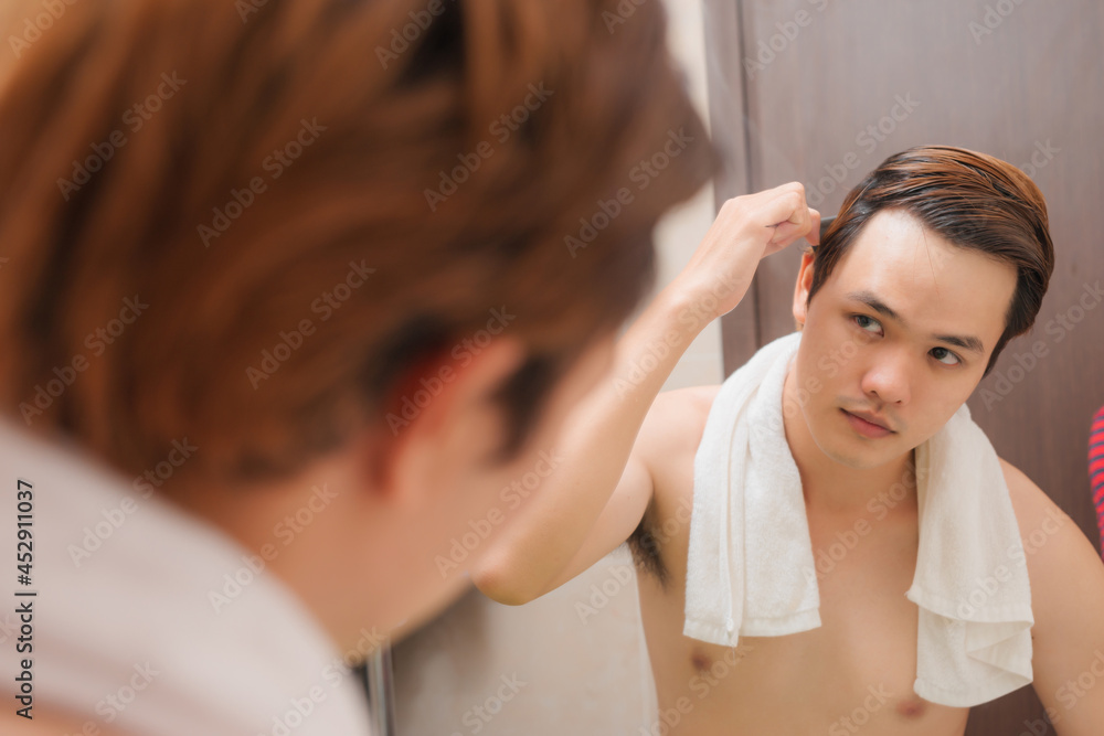 Morning routine. Rear view of handsome young man combing his hair while standing against a mirror Morning routine. Rear view of handsome young man combing his hair while standing against a mirror