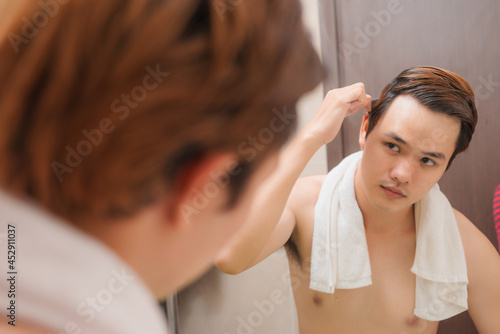 Morning routine. Rear view of handsome young man combing his hair while standing against a mirror