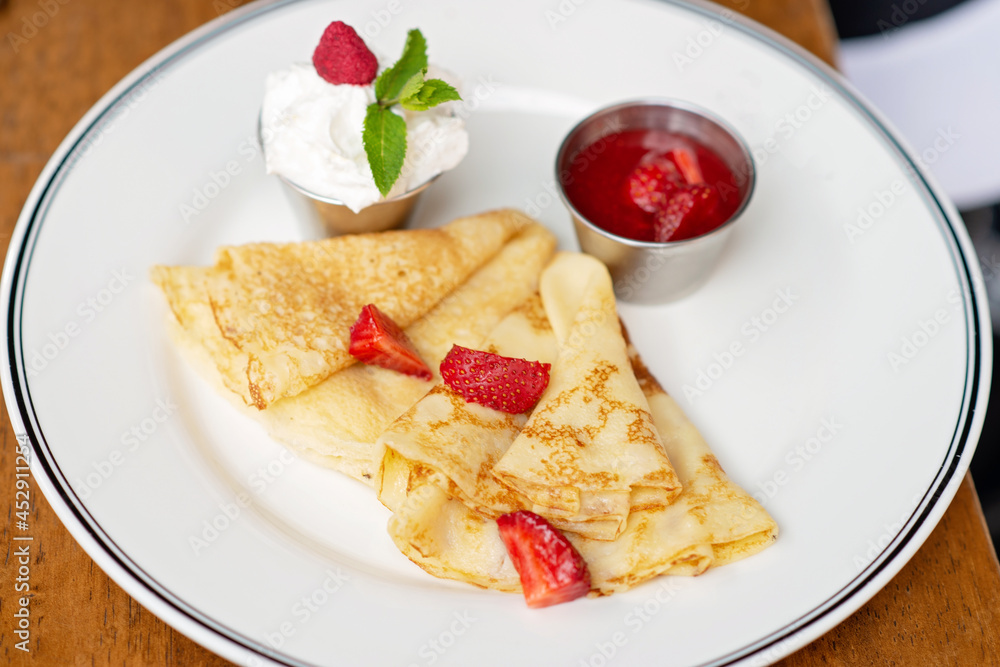 Delicious crepes with fresh strawberries, mint leaves and sour cream espuma. Breakfast at the restaurant. Soft selective focus. Delicious crepes with fresh strawberries, mint leaves and sour cream espuma. Breakfast at the restaurant. Soft selective focus.