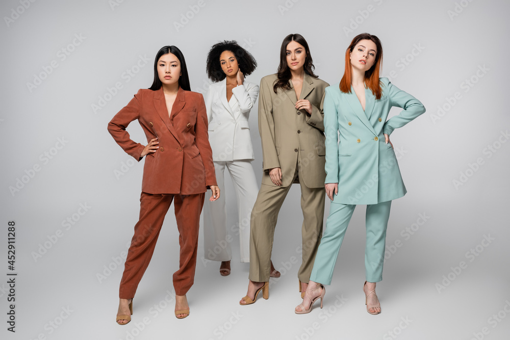 full length of multiethnic models in pastel color suits posing on grey full length of multiethnic models in pastel color suits posing on grey