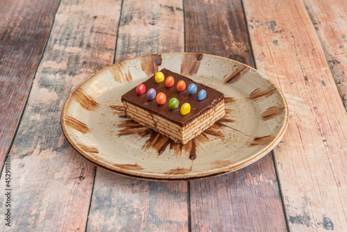 Portion of chocolate cake with cookies, nutella and chocolate dragees of assorted colors on wooden table