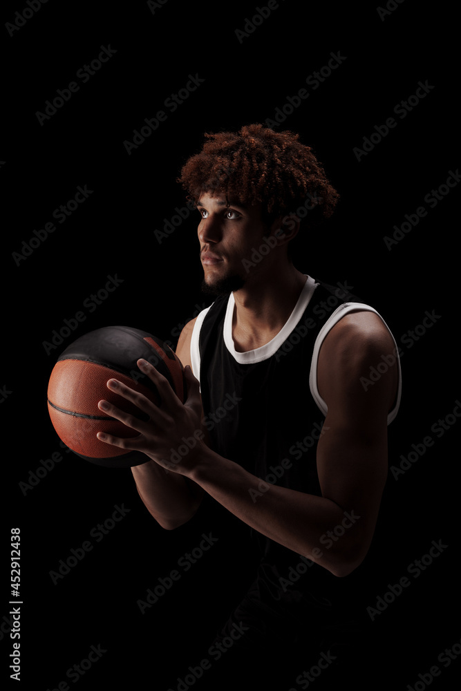 Professional basketball player holding a ball against black background. Serious concentrated african american man in sports uniform Professional basketball player holding a ball against black background. Serious concentrated african american man in sports uniform