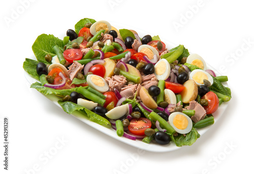Traditional Nicoise salad in a white rectangular salad bowl isolated on white background.