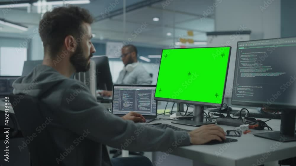 Multi-Ethnic Office: White IT Programmer Working on Computer with Green Screen Chroma Key Display. Male Software Engineer Developing App, Program, Video Game. Terminal with Code Language. Static Shot Multi-Ethnic Office: White IT Programmer Working on Computer with Green Screen Chroma Key Display. Male Software Engineer Developing App, Program, Video Game. Terminal with Code Language. Static Shot