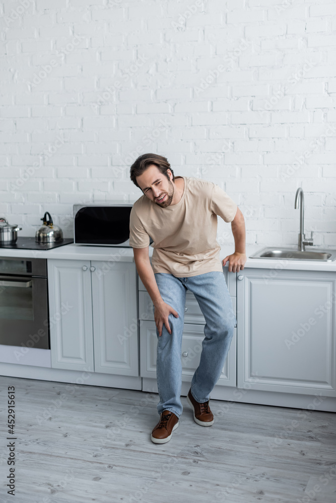 Diseased man touching knee on kitchen Diseased man touching knee on kitchen
