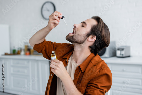 Side view of man taking cbd oil at home photo