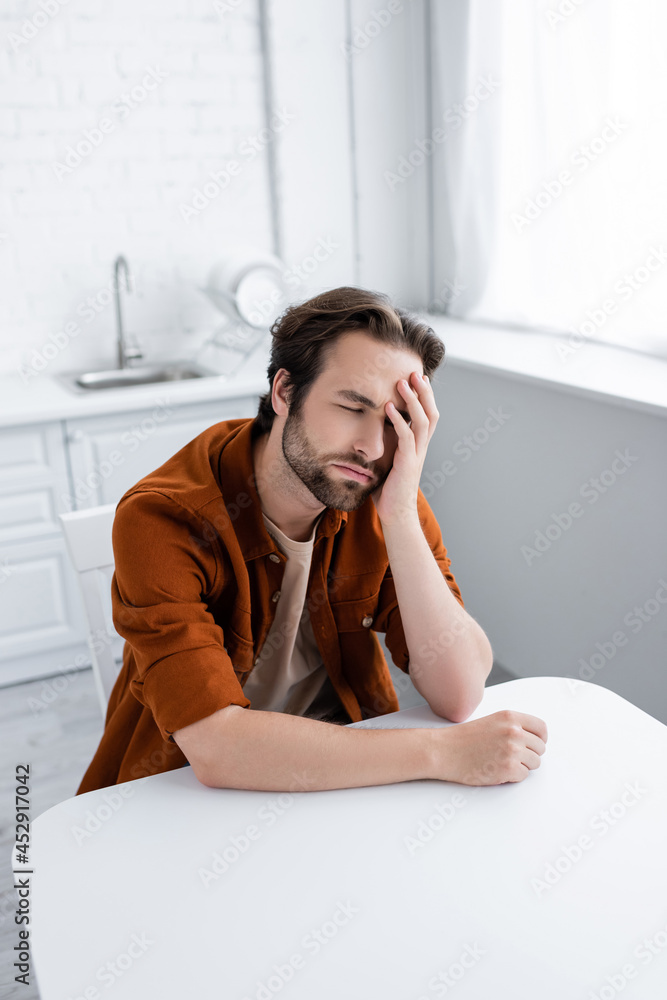 man sitting at kitchen table and suffering from migraine man sitting at kitchen table and suffering from migraine