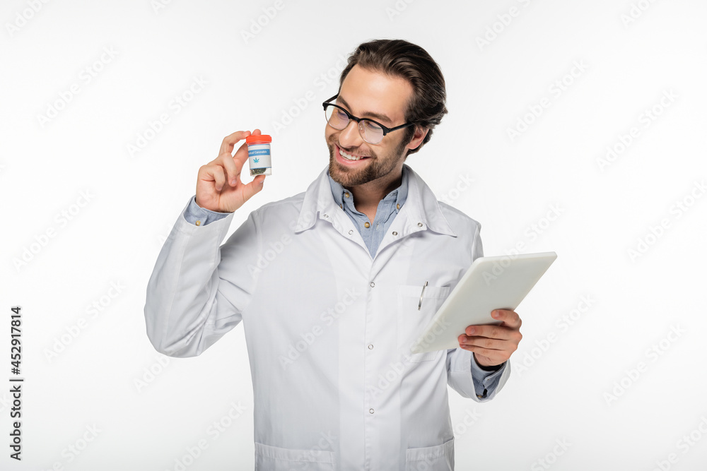 smiling doctor holding digital tablet and container with dry medical cannabis isolated on white smiling doctor holding digital tablet and container with dry medical cannabis isolated on white
