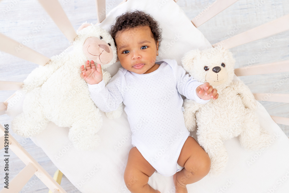 cute African-American little baby in white sleeping bed with bear toys