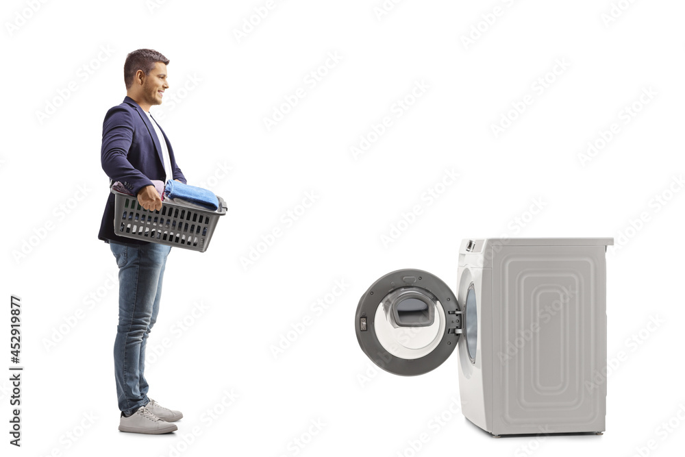 Full length profile shot of a man with a laundry basket standing in front of a washing machine - obrazy, fototapety, plakaty 