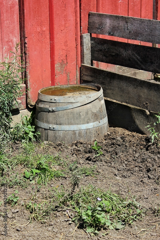 Old wooden barrel submerged in mud in the barnyard next to a red wall.