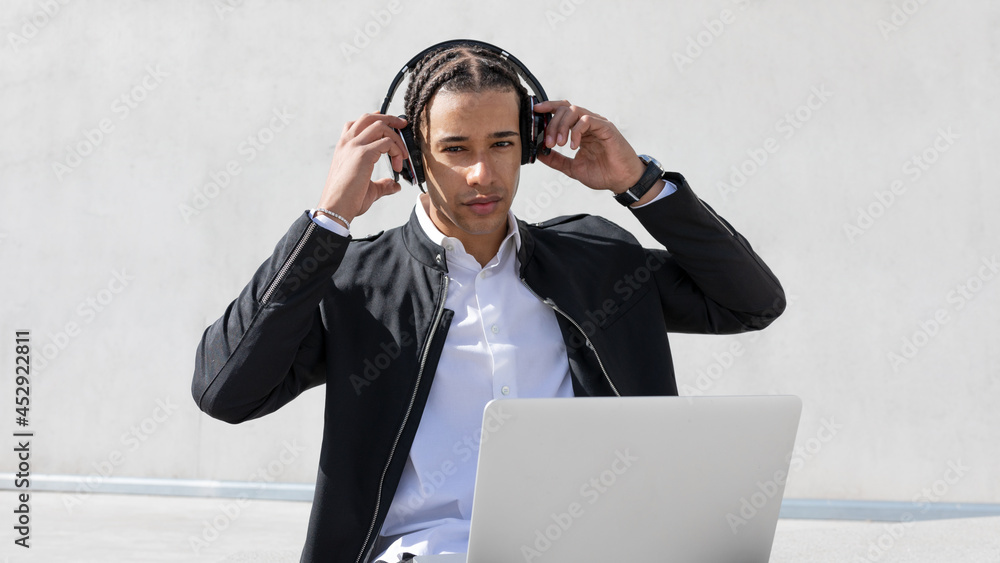 Ethnic businessman with laptop and headphones on street Ethnic businessman with laptop and headphones on street