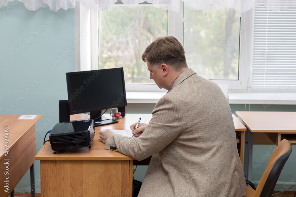 A professor at the institute at his desk by the window writes assignments for his students. A professor at the institute at his desk by the window writes assignments for his students.