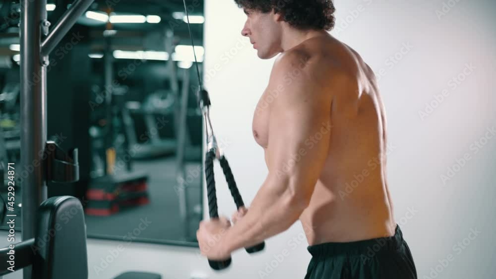 Male bodybuilder doing down pulls for triceps workout. Side view, camera zooms in on athlete. Male bodybuilder doing down pulls for triceps workout. Side view, camera zooms in on athlete.