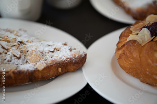 an almond croissant and a bun with strawberry slices lie on a white plate next to a white cup of coffee cappuccino and latte food fresh pastries bakery handmade kitchen cafe breakfast health