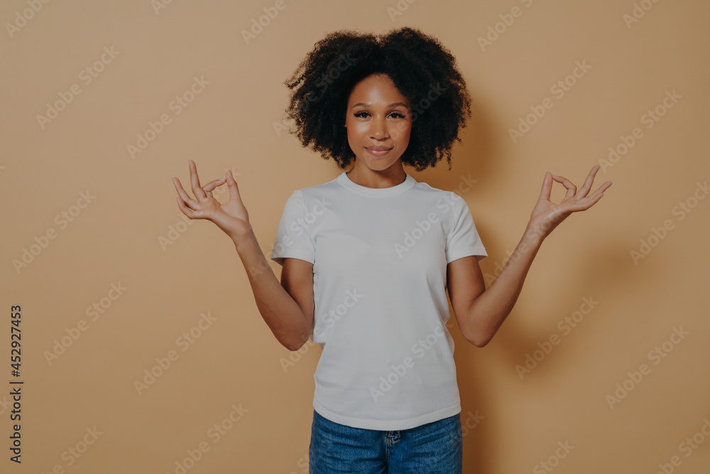 Peaceful afro american young woman keeping hands in mudra gesture, isolated on beige wall Peaceful afro american young woman keeping hands in mudra gesture, isolated on beige wall