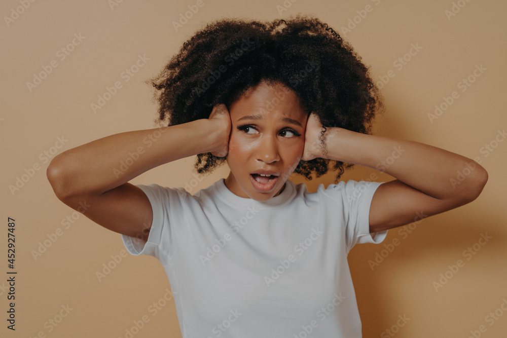 Young annoyed african woman covering her ears and keeping mouth opened isolated on beige background Young annoyed african woman covering her ears and keeping mouth opened isolated on beige background