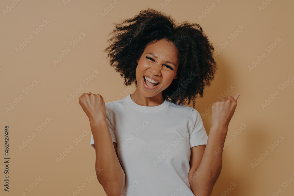 Young euphoric woman clenching fists and celebrating achievement, isolated on yellow background Young euphoric woman clenching fists and celebrating achievement, isolated on yellow background