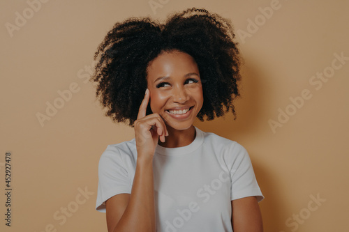 Pensive african woman with curly hair touching temple with forefinger, isolated on beige background
