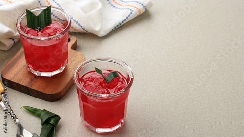 Manisan Kolang-Kaling (Preserved Sugar Palm Fruit) with Red Color. Served in a Glass with Wooden Coaster and Pandan Leaves as Garnish. photo