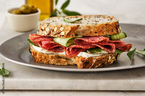 Sandwich with salami sausage and cucumber on marble background.