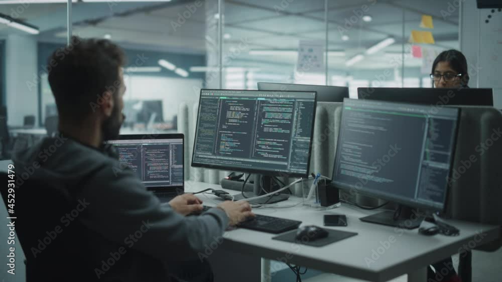 Diverse Office: IT Programmer Working on Desktop Computer. Male Specialist Creating Innovative Software Engineer Developing App, Program, Video Game. Terminal with Coding Language. Over Shoulder