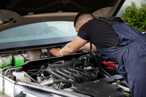 a man repairs a car. a man in blue special clothes to repair the car. engine parts machine repair maintenance breakage problem hands people man master