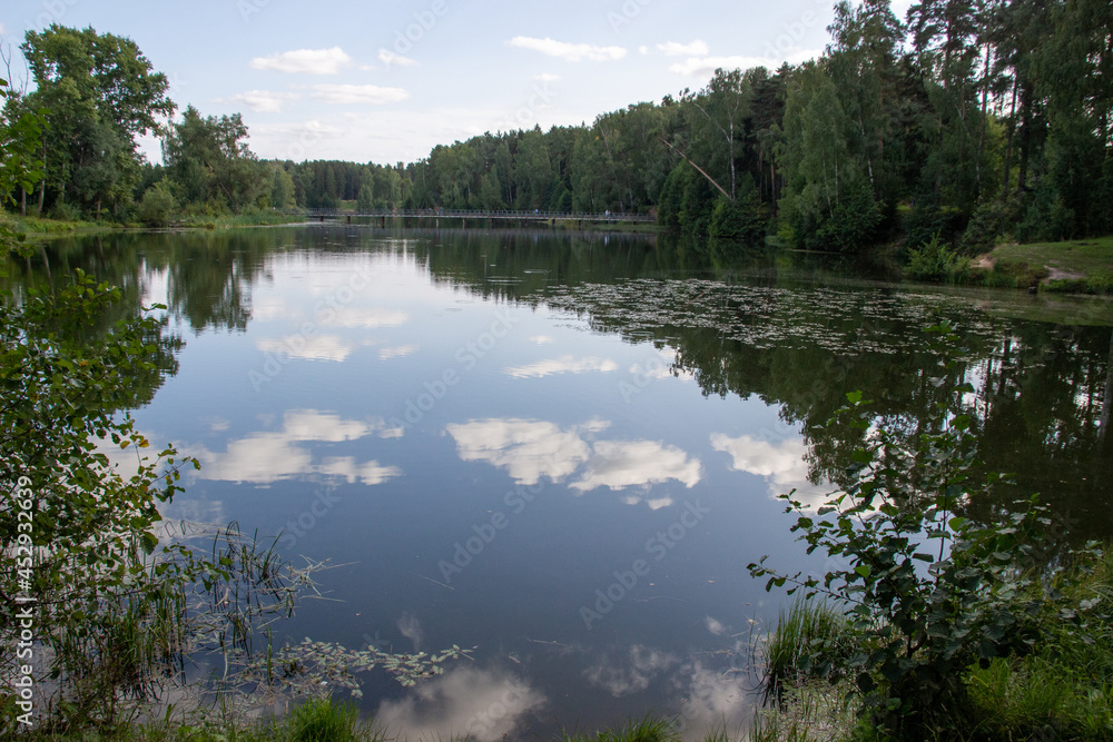 Summer forest landscape with calm river reflecting blue sky and clouds