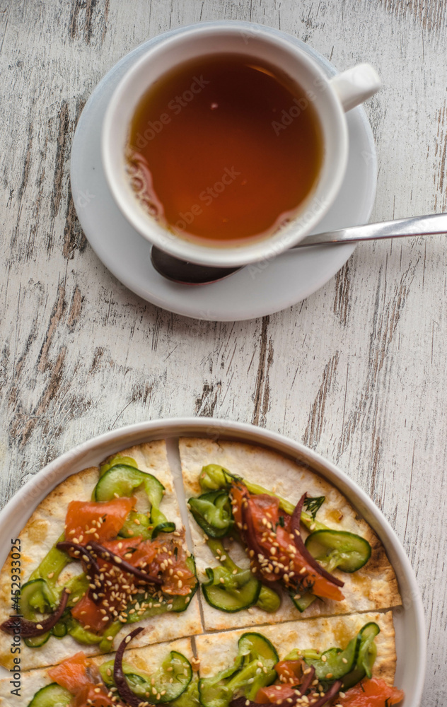 bread tortilla with salmon cucumber sauce and sesame along with tea on a white wooden background. healthy food background texture pita with red fish vegetables and sesame sprinkles. bread tortilla with salmon cucumber sauce and sesame along with tea on a white wooden background. healthy food background texture pita with red fish vegetables and sesame sprinkles.