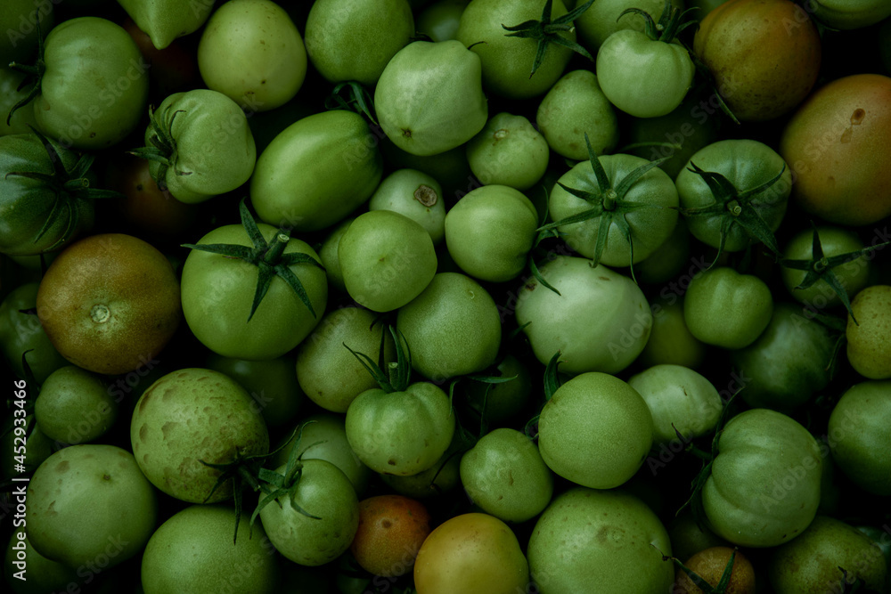 Green tomato (unripe) in wicker basket on wooden background. Unripe green tomato in bowl for fried dish or salted pickled vegetables. Raw green tomato on table for dinner Green tomato (unripe) in wicker basket on wooden background. Unripe green tomato in bowl for fried dish or salted pickled vegetables. Raw green tomato on table for dinner