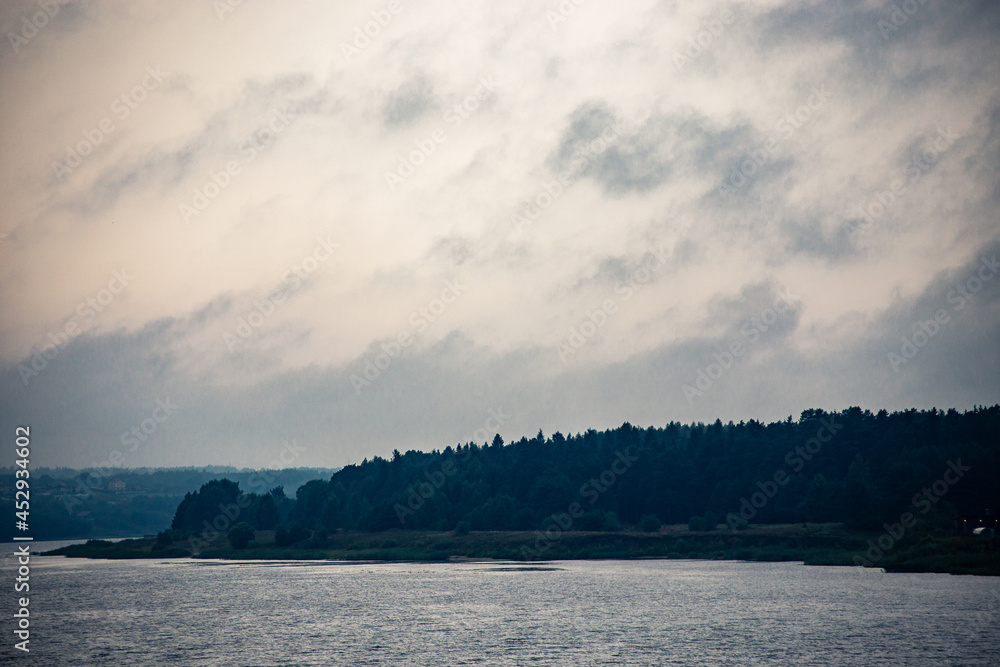 Obraz premium River landscape. Calm water and with clouds. Trees grow on the nearest shore. There is copy space