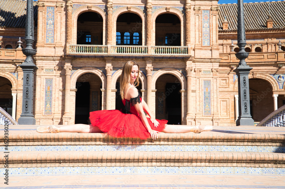 classical ballet dancer in red tutu with her legs open on the steps of a park and her arms outstretched. Classical ballet.