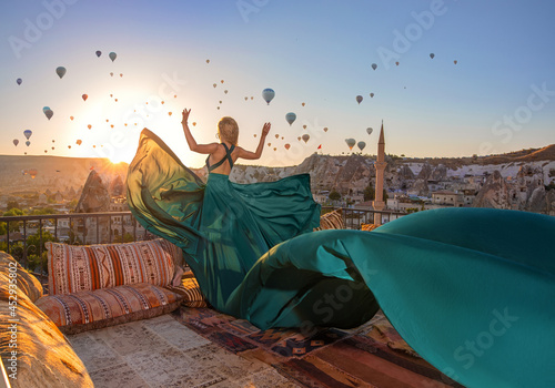 Beautiful blonde girl in the long green dress in Cappadocia sunrise on the amazing background of hundred flying balloons. © Taranukhin Alex