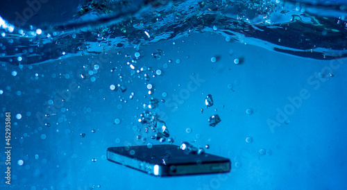 black and white phone dropped into the water. phone in water.phone in water bubbles.phone sinks in water
