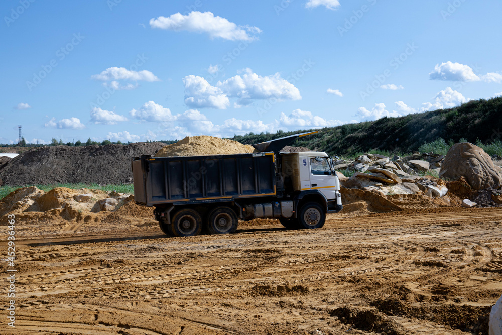 Obraz premium Dump truck transports sand in open pit mine. Excavator on the development of sand in a quarry. Mining industry concept