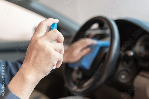 Close up hand a man press the spray bottle alcohol into the cloth to clean the steering wheel Prevent pathogens from contamination
