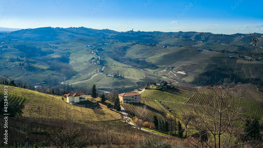 View from above on rural houses on the hill among colorful autumnal vineyards and trees in Piedmont, Northern Italy