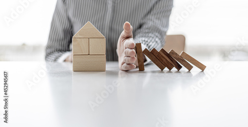 Obraz na plátne Woman using her hand to prevent wooden blocks from falling onto wooden blocks in the shape of a house, insurance to prevent risks that will save us high prices, home insurance ideas