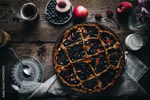 Rustic peach-blueberry-ricotta spelt pie on old wooden table served with coffee and fruits.