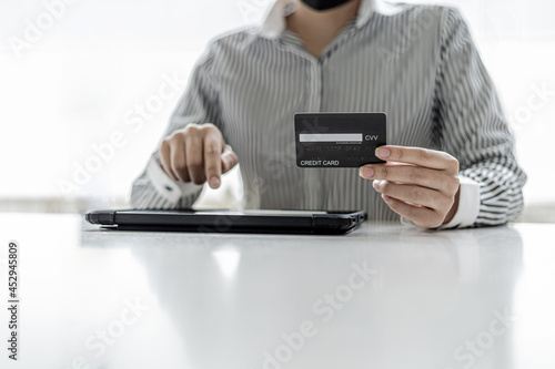 A woman holding a credit card and touching a tablet, she is filling out her credit card information to pay for an order on an online shopping site. Online shopping and credit card payment concept.