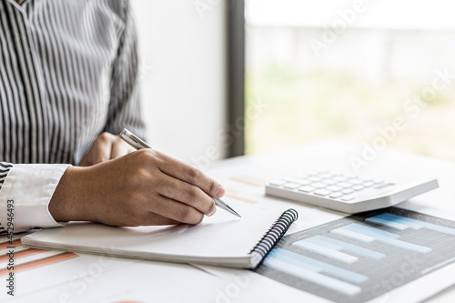 A businesswoman is taking notes in a notebook, she checks company financial documents and she takes corrective reports to the finance manager for correction. Finance concept.