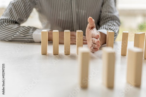 Women put their hands between wooden blocks, wooden blocks arranged in dominoes, likened to running a business well and solving problems. The concept of business management on risk. photo