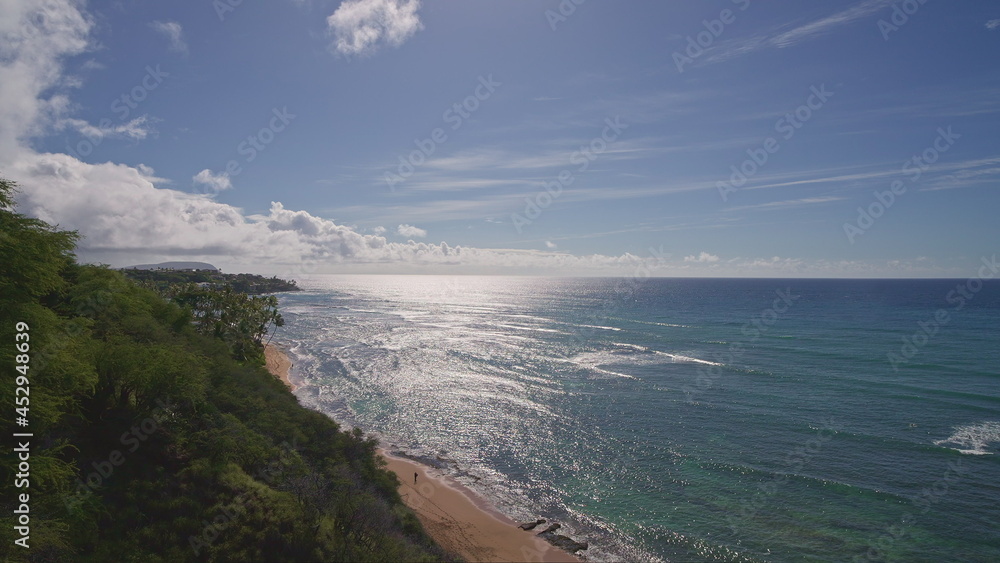 View from above to Diamond Head Beach Park. People swim in the ocean. Yellow sand on the beach on the tropical island of Oahu Hawaii. The turquoise color of the Pacific Ocean water.