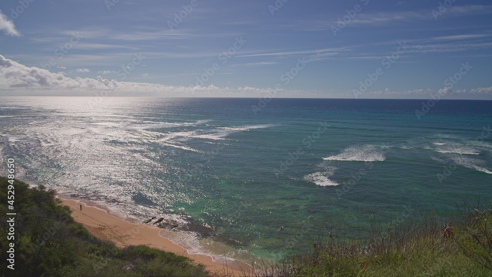 View from above to Diamond Head Beach Park. People swim in the ocean. Yellow sand on the beach on the tropical island of Oahu Hawaii. The turquoise color of the Pacific Ocean water.
