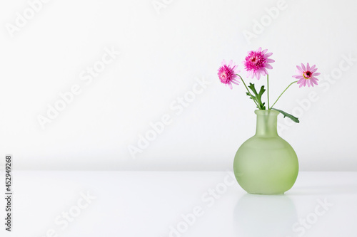 Pink flowers in green vase on white table. Front view.